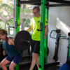 Trening z trenerem-personalnym a także trening z trenerem personalnym w parach w Gdańsku. Trener asystuje przy podnoszeniu przez dziewczynę ciężkiej sztangi.